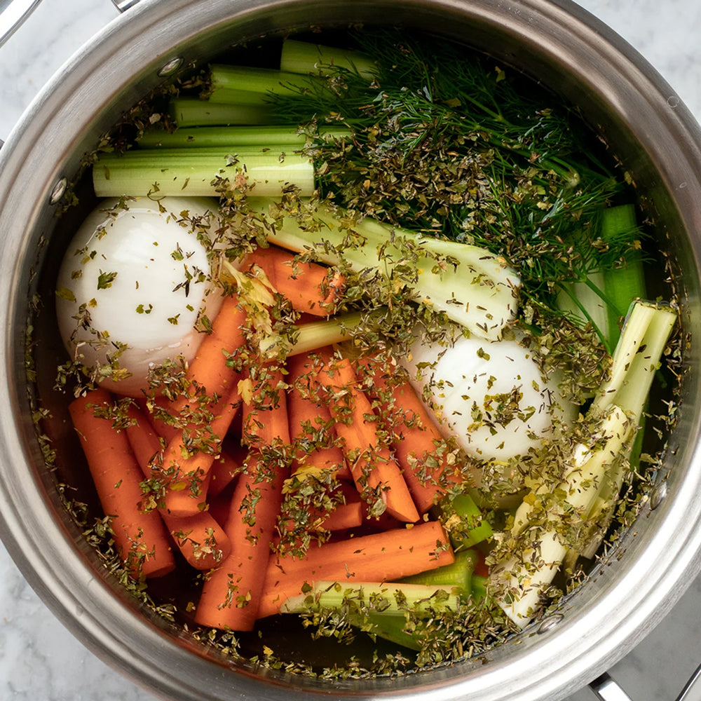 Ingredients for a vegetable broth including carrots, celery, and herbs in a pot.