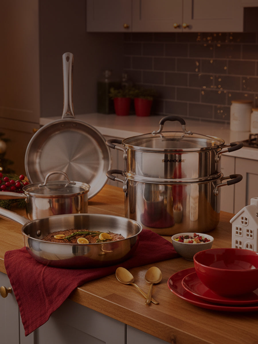 Stainless steel cookware set on a kitchen counter with red dishes and utensils.